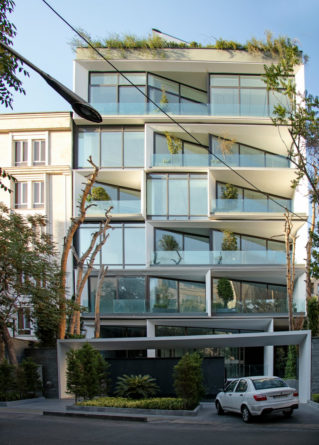 Modern apartment building with glass balconies and greenery exterior.