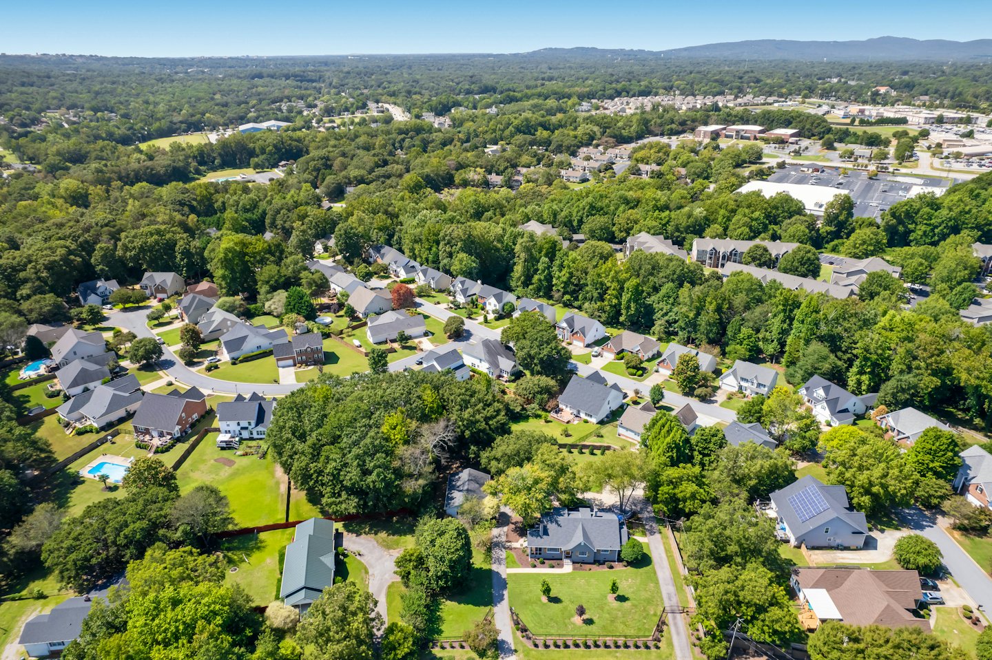 Aerial view of suburban homes with grey roofs and green trees.